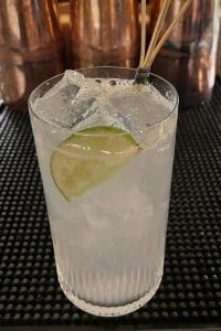 a fizzy light drink in a highball glass filled with ice cubes and a lime wedge inside