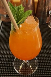 an orange coloured cocktail in a beer tasting glass with a mint sprig and straw inside